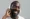 Um homem sorridente, usando fones de ouvido azuis e brancos, apreciando música com expressão de alegria e satisfação.