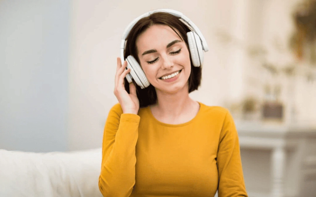 Mulher sorridente usando fones de ouvido sem fio branco, apreciando música em um ambiente aconchegante.